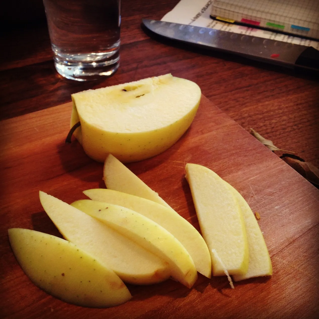 Manzana amarilla cortada en gajos sobre una tabla de madera, lista para trocear